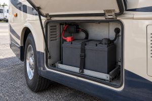 Large AGM-style battery secured in a motorhome exterior service bay, with insulated posts and a covered fuse beside the case